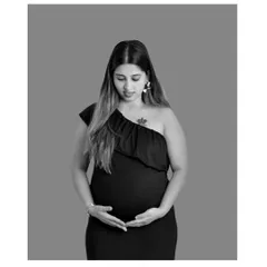 A quiet, contemplative moment captured in black and white. The mother-to-be looks down at her bump with a gentle expression, creating a portrait filled with love and anticipation.