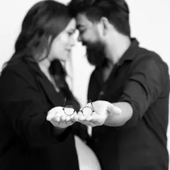 A close-up version of the couple holding the tiny glasses. This intimate, modern portrait focuses on the detail and the couple's connection, making it a perfect pregnancy announcement photo.