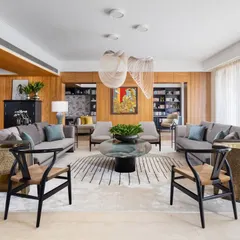 A frontal view of the Magnolia living room, showcasing the symmetry and balance in the furniture arrangement. The two wishbone chairs in the foreground add a touch of mid-century modernism, while the custom rug anchors the central seating area.