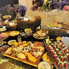 A beautiful grazing table designed for a special birthday celebration. The spread includes caprese skewers, various cheeses, dips, and breads, all surrounded by gorgeous floral arrangements.