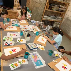 A class of adult students learning watercolor techniques, each practicing floral motifs on their boards.