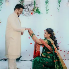 A sweet reversal, with the bride kneeling to put a ring on the groom's finger, both sharing a happy smile.