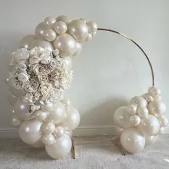 A minimalist and chic decorative arch. This piece combines a simple metal frame with an arrangement of pearl white balloons and a beautiful bouquet of white artificial flowers, perfect as a photo booth or entrance decor for an elegant event.