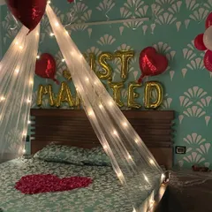 A romantic 'Just Married' room setup. The decor features a bed canopy with fairy lights, red and white balloons, and a heart made of rose petals on the bed.
