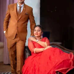 A classic and formal indoor portrait. The bride's flowing red gown and the groom's sharp suit create a look of elegance and sophistication.
