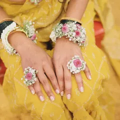 A close-up of the bride's hands, showing the detailed hath phool and floral rings. The design combines pink flowers with baby's breath and pearl accents, matching the rest of her Haldi jewellery.