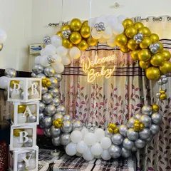 A 'Welcome Baby' decoration for an intimate home setting. This design uses a full ring of silver, gold, and white balloons, a neon sign, and 'BABY' blocks.
