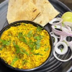 A classic plate of Paneer Bhurji, garnished with fresh coriander and served with sliced onions and a lemon wedge.