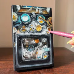 Adding the final touches to the miniature painting of a chaotic sink. The tiny brush allows for incredible detail, even on such a small canvas.