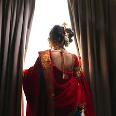 A moment of anticipation. The bride, seen from behind, looks out the window, her silhouette framed by the curtains.