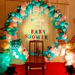 A traditional Marathi baby shower, also known as 'dohale jevan'. The setup includes a circular balloon arch and a special chair for the mother-to-be, with a sign that reads "Kunitari yenar ga" (Somebody's coming).