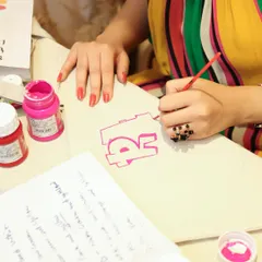A close-up of me painting a custom initial onto a canvas tote bag at a pop-up event. This kind of on-the-spot personalization is a huge draw and makes for a great guest experience.