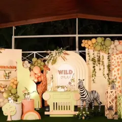 An expansive "Wild One" jungle safari theme for a first birthday. This full-stage decoration includes multiple backdrops with giraffe print, custom arches, a dessert cart, and life-sized animal props like a zebra and elephant to create an immersive experience.