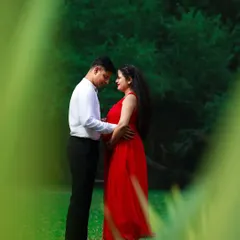 An intimate moment between expectant parents during an outdoor maternity session. The vibrant red dress adds a beautiful pop of color against the lush green background.