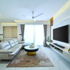 A modern living room where the TV wall combines a marble-finish panel with fluted details and warm backlighting. The space is designed to feel clean and airy, with a large sectional sofa providing ample comfort.