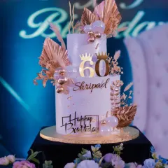 This elegant two-tier cake was for a 60th birthday, designed with a classic white and gold theme. It's adorned with golden palm leaves, delicate baubles, and custom toppers to celebrate the milestone.