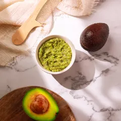 A DIY recipe shoot featuring an avocado hair mask. The styling with a wooden comb and marble background creates a natural, self-care aesthetic.