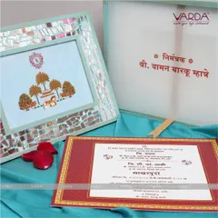 A unique invitation concept featuring a framed artwork with a traditional Indian motif and a mirrored border. This reusable frame is paired with a classic red and gold invitation card.