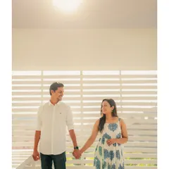 A simple, happy moment between Annalisa and John, holding hands against a backdrop of white louvers with the sun flaring above. The feeling is light, airy, and joyful.