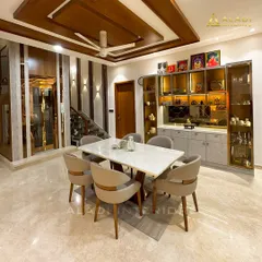 This dining space exudes luxury with a marble-top table, plush upholstered chairs, and a stunning glass crockery unit with internal lighting. The wooden ceiling panels and intricate wall details add layers of warmth and sophistication.