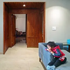 A view into a Gurgaon residence where stained pine wood panels create a warm, rhythmic entryway. The design divides a larger volume into smaller, functional 'pockets' without using solid walls.
