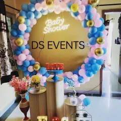 A simple yet beautiful baby shower setup perfect for home celebrations. The circular balloon arch in pink, blue, and gold frames the space, while the tiered stands are ready for the cake and gifts.