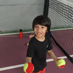 The joy of tennis starts here. This little champ from our Red Batch is all smiles, holding the special red balls we use for our youngest players to learn control.