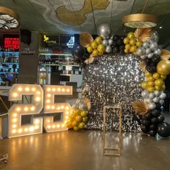 For a 25th anniversary party, I created this glamorous photo corner. It includes a shimmering silver sequin backdrop, large light-up '25' marquee numbers, and a custom balloon arch in a sophisticated black, gold, and silver color scheme.