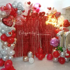 We designed this vibrant 10th-anniversary decoration with a red tinsel backdrop, a 'Happy Anniversary' neon sign, and a balloon arch in red, silver, and rose gold for a romantic celebration at home.