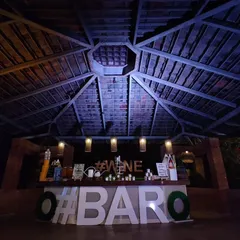 This rustic bar setup was designed to complement the venue's open-air gazebo structure. The large '#BARO' lettering adds a bold, modern touch to the otherwise natural and earthy theme.