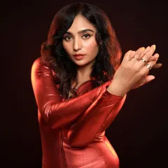 A dynamic studio shot using a vibrant red outfit and warm, smoky background to create a sense of energy and movement. The lighting highlights the metallic texture of the fabric.