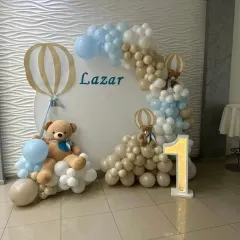This teddy bear and hot air balloon theme for Lazar's first birthday uses a neutral and blue color palette. The setup includes a circular backdrop, a light-up number '1', and cute bear details.
