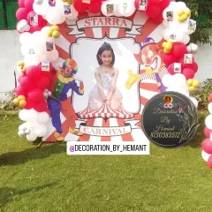 A close-up of the personalized carnival theme backdrop. It features a large photo of the birthday girl, fun clown illustrations, and is framed with red and white balloons, with small photos clipped on for a personal touch.