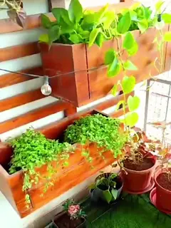 Artificial grass underfoot, a wooden slat wall with two big wooden planter boxes of pothos and trailing plants hung on it, a string of bulbs and terracotta pots by a netted railing