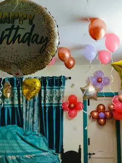 Balloons in a bedroom: copper, pink, lilac and red balloons on the ceiling with ribbons hanging, flowers made of balloons on the wall, gold star foils and a round Happy Birthday foil