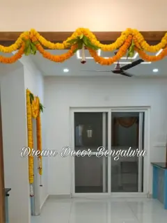 An inside doorway in a new flat framed with yellow and orange marigold strings and mango leaves, with more marigold on a second doorway behind