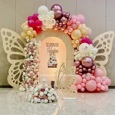 A beautiful butterfly-themed First Holy Communion decoration. This setup features large butterfly wing cutouts, a pink and white balloon arch, and floral arrangements.