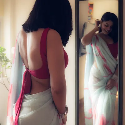 An intimate portrait using a mirror to tell a story of self-reflection. The soft, natural light from the window highlights the texture of the saree and creates a gentle, film-like mood.