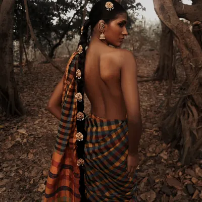A portrait from an outdoor editorial, set against the rich textures of banyan tree roots. The earthy tones and natural setting create a raw and powerful image that feels deeply connected to nature.