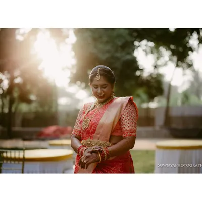 A serene bridal portrait captured in the soft morning light. The bride, in her beautiful red saree, is having a quiet moment of reflection before the ceremony begins.