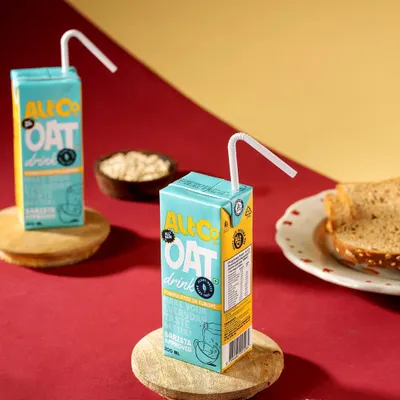 A graphic and colorful studio shot of Alt Co. Oat Drink. The bold red and yellow background with wooden coasters creates a modern, pop-art feel that is eye-catching and playful.