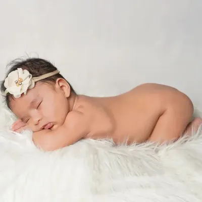 The classic newborn pose. This baby is sleeping peacefully on a soft white fur rug, a simple and timeless portrait that highlights their delicate form.