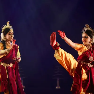 A dynamic pose from "Shrishti Stithi Laya". The dancers' powerful leg extensions and synchronized mudras capture the fierce energy of the cosmic dance. The matching red and gold costumes create a visually unified and striking look.