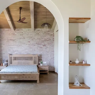 An arched entryway frames the view into a serene bedroom in our 'Ekaant' villa. The design combines an exposed brick wall, a wooden ceiling, and custom furniture to create a space that feels both rustic and luxurious.