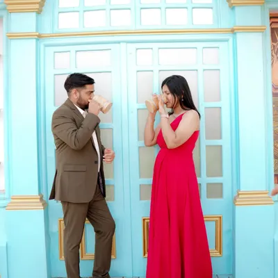A playful moment sharing a drink against a vibrant blue door, reminiscent of a European street. The woman's bright red dress pops against the cool tones, creating a lively and stylish pre-wedding photo.