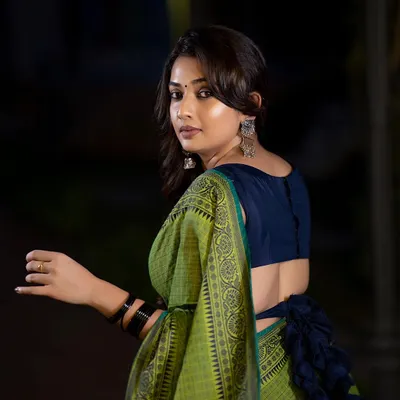 A beautiful outdoor portrait at dusk. The low light and backlighting create a soft glow around the subject, highlighting the elegant drape of the green and blue saree.