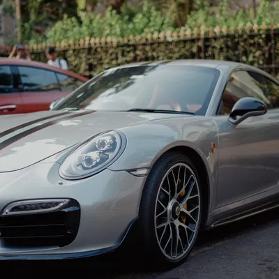 A sleek silver Porsche 911 with black racing stripes, parked on a city street. This shot captures the aggressive lines and high-performance look of a modern supercar.