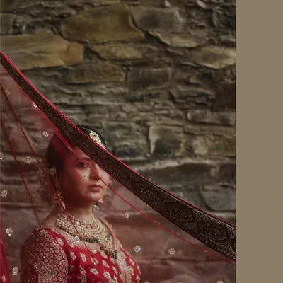A classic bridal portrait with the veil gently obscuring her face, creating a sense of mystery and timeless beauty. The rustic stone wall provides a beautiful textured background for this shot from a Udaipur wedding.