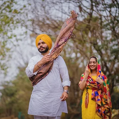 Draped in tradition and love. This shot captures a playful moment between Kanwal and Avneet, with his beautifully patterned shawl and her colorful phulkari dupatta adding a vibrant touch to their outdoor pre-wedding session.