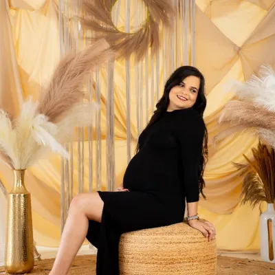 A relaxed and happy solo portrait in our boho studio. The mom-to-be, dressed in a simple black dress, smiles warmly, capturing a moment of pure contentment.